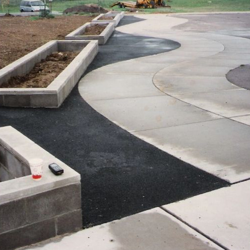 The completed masonry flower boxes finished and planted, bordering a curved concrete and asphalt walkway at the school entrance
