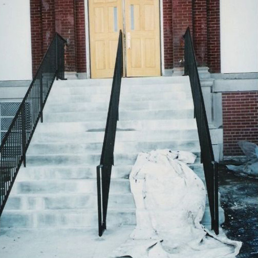 The rebuilt concrete entrance stairs finished and in service, flanked by new black steel handrails